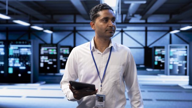 Admin in server hub checking recovery plan on tablet, monitoring data center energy consumption across components, making sure sensors are functioning optimally, doing routine disk checks